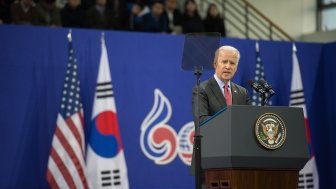 Joe Biden stands at a podium delivering a speech in front of U.S. and South Korean flags