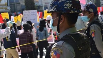 Two soldiers in miliary uniform watch a crowd of protestors.