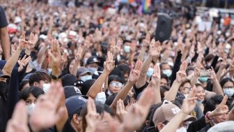 A crowd of people gathered at a protest, lifting their hands with three fingers extended in a gesture of protest against the government.