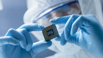 A person in a clean suit holding up a computer chip