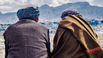 Two men sit with their backs to the camera, looking out at the Afghan mountains.