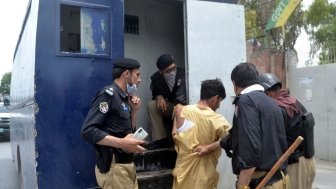 Police officials are pushing a man with torn clothing into the back of a police vehicle after he has been arrested.