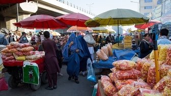 Afghan men and women in traditional clothing shop at an outdoor market.