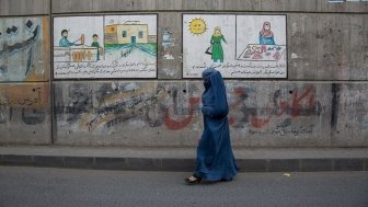 A woman in a blue burqa walks along an empty street in front of murals and graffiti.