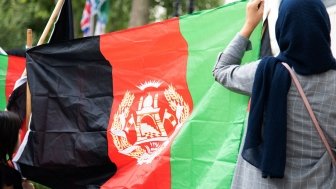 Two people with their backs to the camera are holding a large Afghan flag.