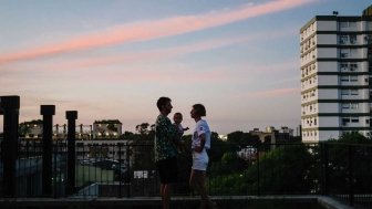 Husband, wife, and baby on balcony overlooking city 