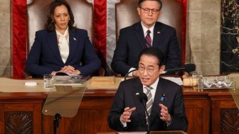 Prime Minister Kishida stands at a lecturn giving a speech, Vice President Harris and Speaker Johnson are seated behind him.