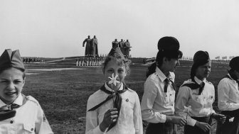 A black-and-white portrait of Soviet Young Pioneers in foreground, with monument to world war two in background