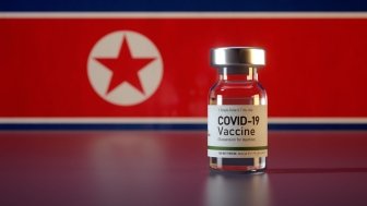 A vial of Covid-19 Vaccine sits in front of the flag of North Korea.