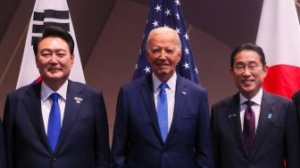 President Yoon, President Biden, and Prime Minister Kishida stand in front of their respective countries flags.