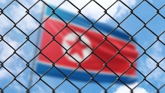 A blurry image of the flag of North Korea behind a chain link fence.