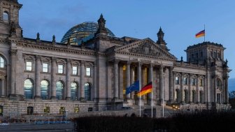 The Bundestag building at dusk, with German and EU flags waving in front. 