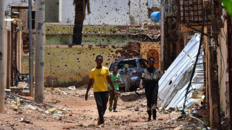 Young people walk along a street marked by destruction. A bloody power struggle has been raging in Sudan for more than 16 months, triggering a refugee crisis. Mudathir Hameed/picture-alliance/dpa/AP Images.