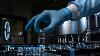 A gloved hand places a vial of medicine in a row