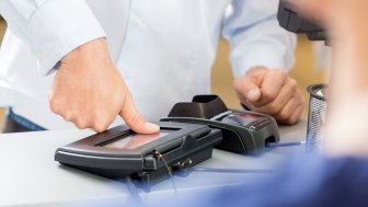 Midsection of customer giving thumb impression to make payment in pharmacy