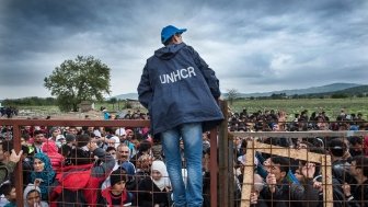 Gevjelija, Macedonia - September 26, 2015. A UNHCR employee talks to refugees as they wait during a rainstorm to enter inside a refugee camp near the town of Gevgelija at the Macedonian - Greek border