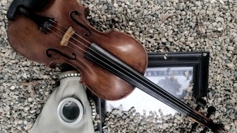 Image of a gas mask, violin and framed photo in gravel