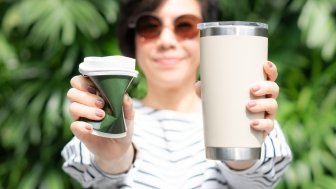 a woman holding one single-use cup and one reusable mug