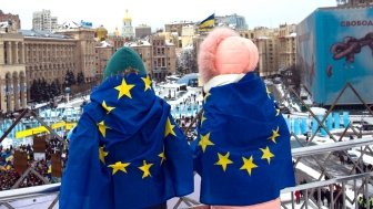 Two people overlooking square with EU flags on their backs