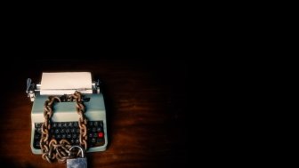 Typewriter locked with a chain and padlock on a black background