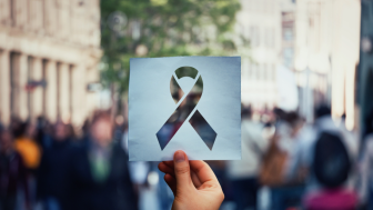 Image of hand holding a paper sheet with HIV red ribbon symbol over crowded street background