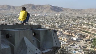 A boy sits on a ledge overlooking Kabul