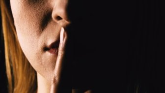 Seriouse woman placing her finger on lips - keep silence or secret. Mouth close up