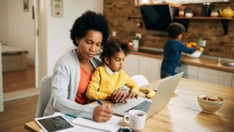 Working mother taking notes while daughter is sitting on her lap. 