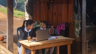 Two girls sitting in front of a computer in the rural outdoors.