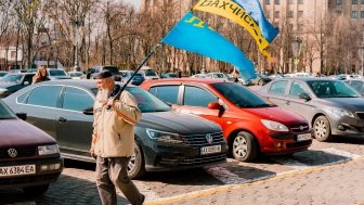 Crimean Tatar man with big beard and traditional cap walks on the city's street with Crimea Tatars and Ukrainian flags. 