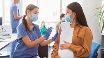 Pregnant woman wearing a mask and receiving a vaccine from a provider in scrubs wearing a mask