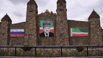 Portrait of Akhmad Kadyrov on a old stone building next to Russian and Chechen Flags