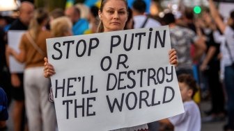 Woman holds a protest sign reading "stop Putin or he'll destroy the world"