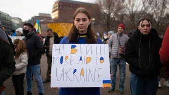 Young Person holding sign with text "Ні війні More Aid To Ukraine"