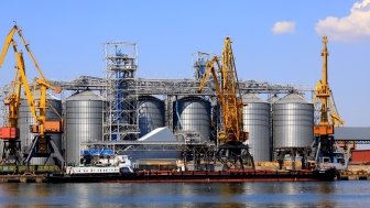 Harbor cranes unload barge at Odesa Seaport amid large metal tanks with wheat, grain, food. 