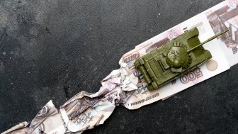 A toy tank runs over Russian ruble notes