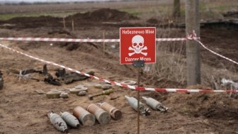 Unexploded ordinance lying in a field next to a red warning sign