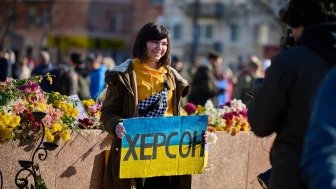 Woman holding sign with colors of Ukrainian flag and "Kherson" written in Cyrillic 