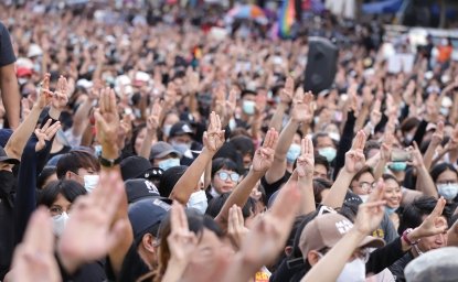 A crowd of people gathered at a protest, lifting their hands with three fingers extended in a gesture of protest against the government.