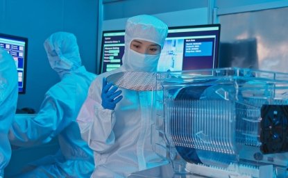 A woman in a clean suit holds up a silicon wafer in a laboratory.