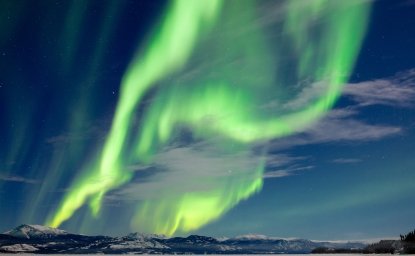 Spectacular Northern Lights or Aurora borealis or polar lights dancing over moon-lit winter landscape of frozen Lake Laberge, Yukon Territory, Canada