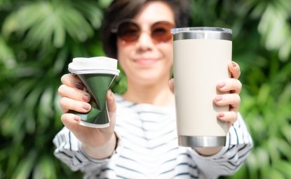 a woman holding one single-use cup and one reusable mug