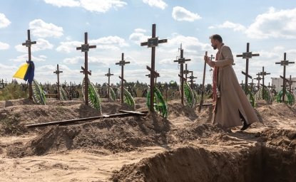 A priest overseas the burial of the remains of 13 unidentified and two identified people who were killed in the Bucha district during the Russian occupation