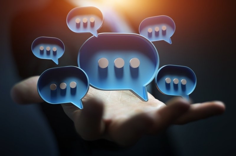 Businessman in dark using digital blue speech bubbles talk icons. Minimal conversation or social media messages floating over user hand. 3D rendering