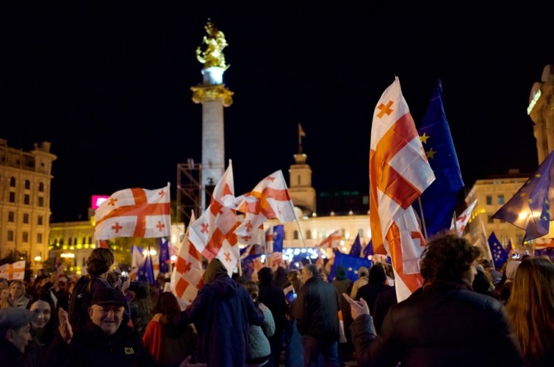 A crowd of protesters in front of the monument in Liberty Square in Tbilisi wave Georgian flags and EU flags. 