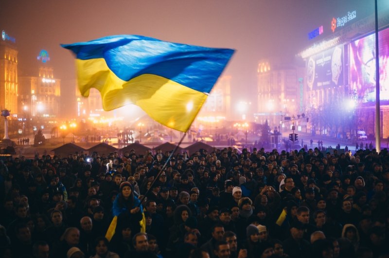 A Ukrainian flag is waved over a busy square. 