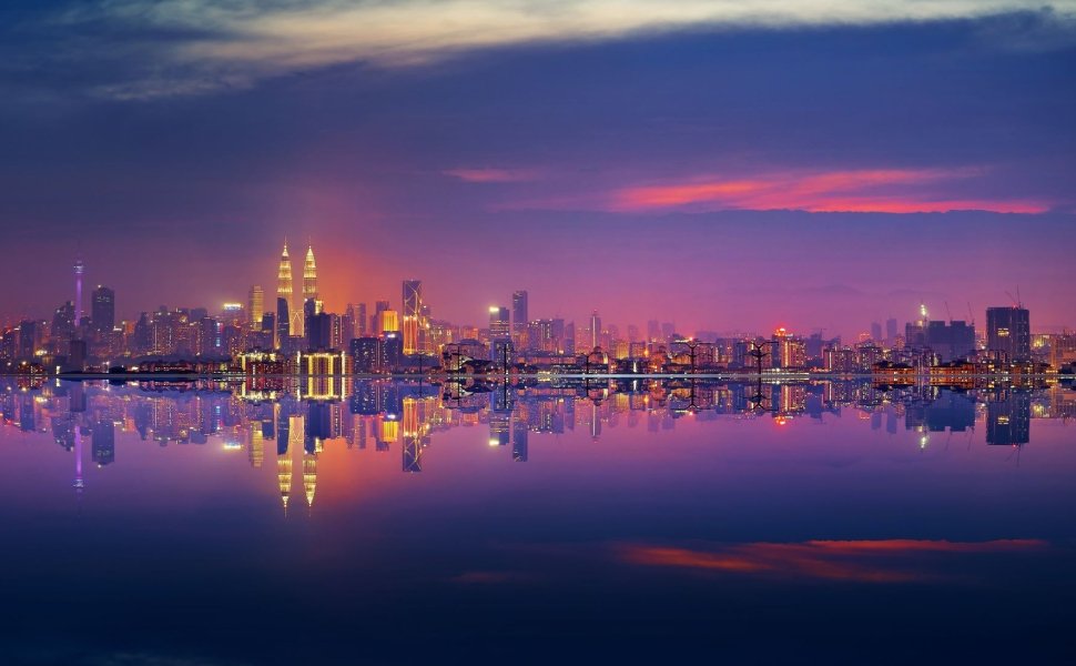 A panoramic shot of the city of Kuala Lumpur at night, seen from the water.