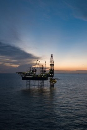 An offshore oil rig in the ocean at sunset.