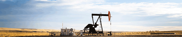 An industrial oil pump jack working on farm land under a morning sky 