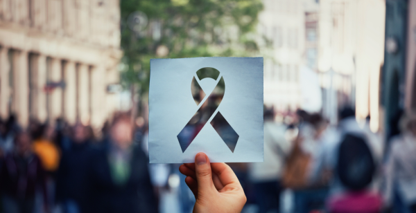 Image of hand holding a paper sheet with HIV red ribbon symbol over crowded street background